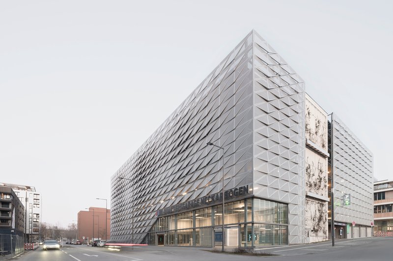Street view showing the glass-walled base beneath the geometric metal-clad volume at dusk