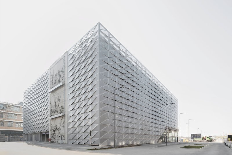 Rear elevation showing the faceted metal envelope and exposed concrete stair tower under grey skies