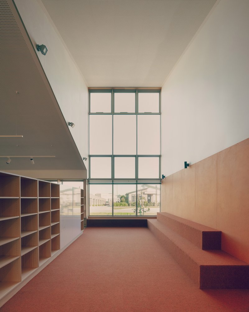 Reading nook with two-story gridded window overlooking the campus and built-in plywood seating along the wall