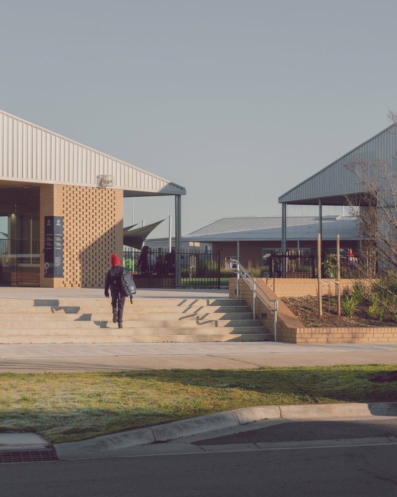 Timber steps and perforated brick retention wall leading between two pavilions with corrugated metal cladding