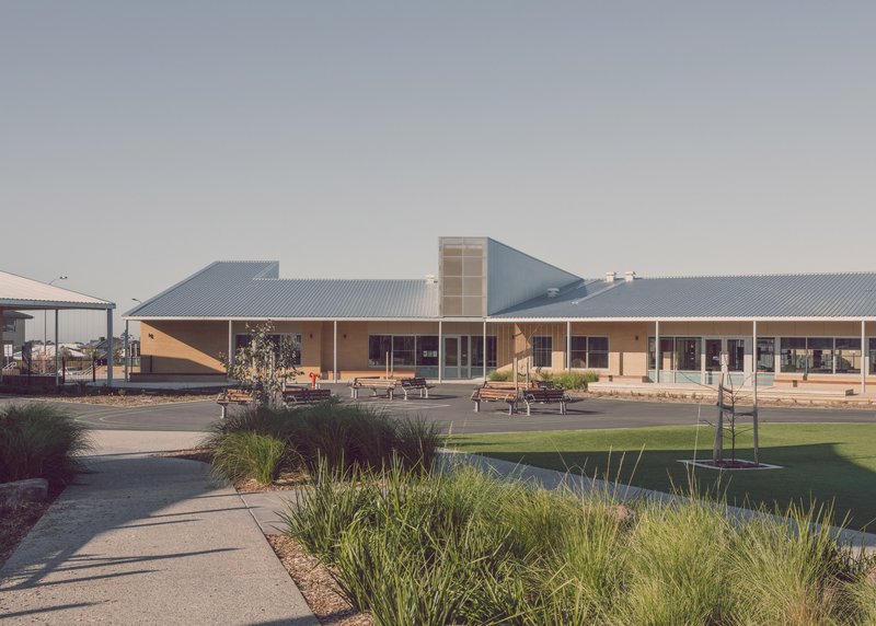 View across landscaped courtyard with native grasses toward the low-slung corrugated metal roofed school complex