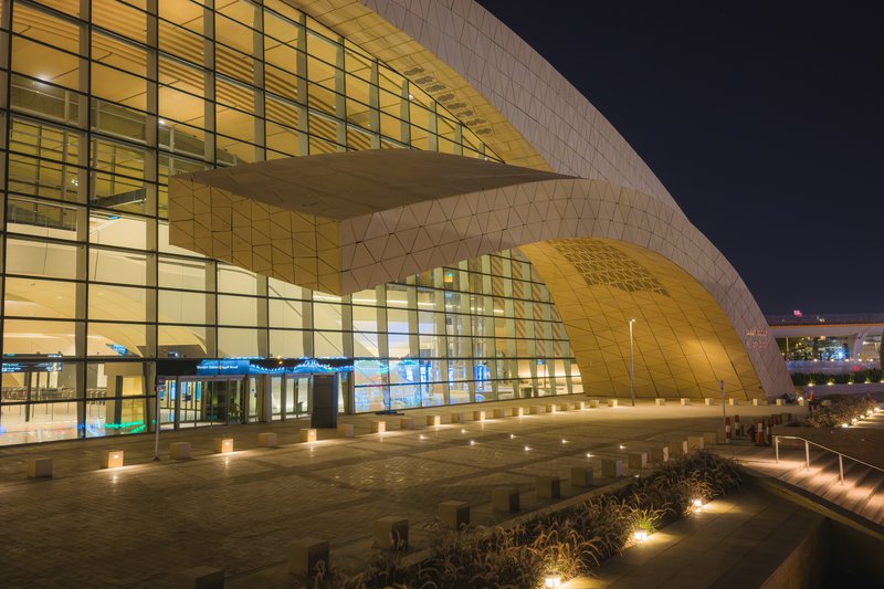 Night view of the tiled facade with illuminated glass curtain wall and landscaped reflecting pool at entry