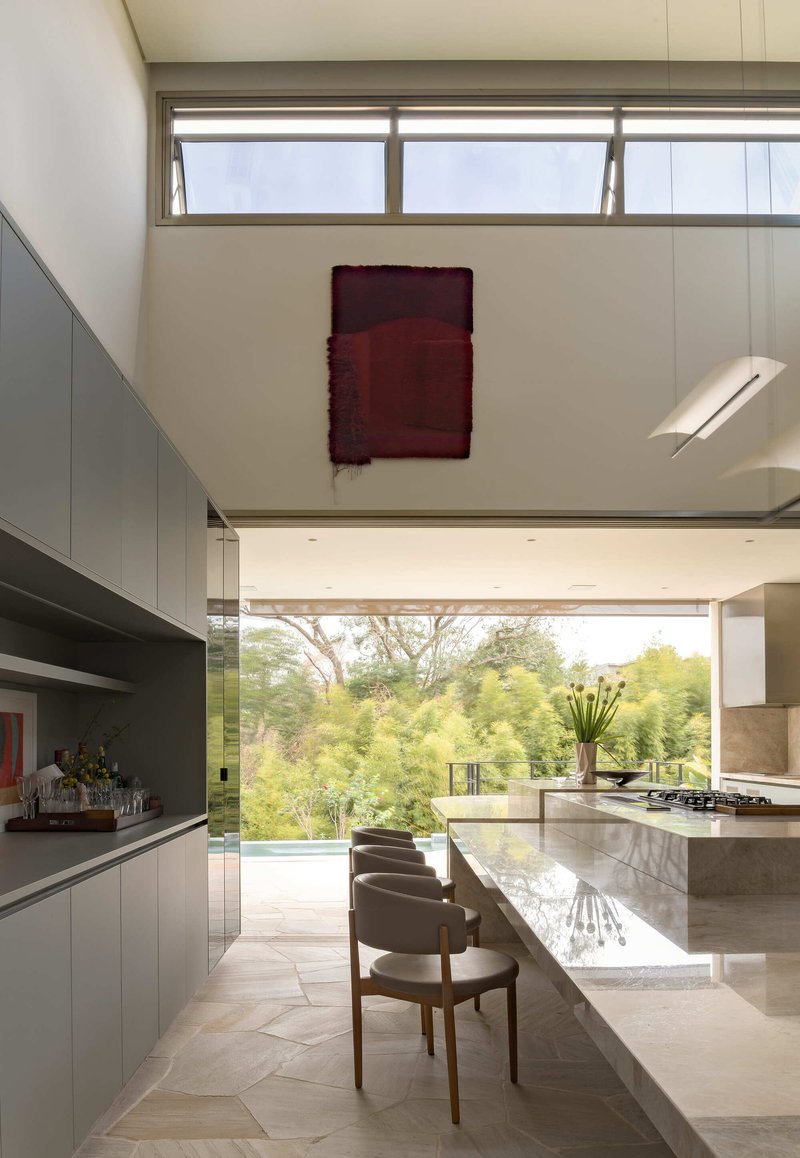 Double-height kitchen with marble island and clerestory windows opening to lush garden beyond