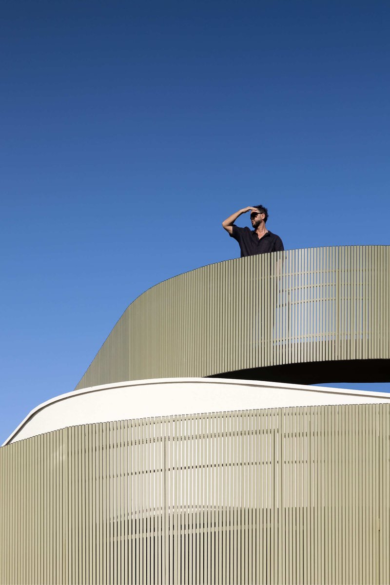 Curved roof terrace clad in vertical metal fins with a person standing against blue sky