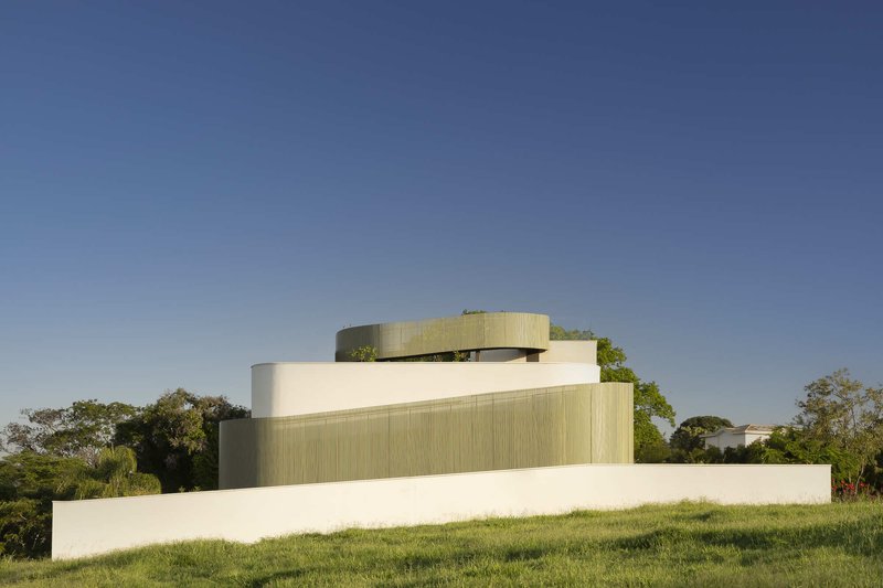 Rear elevation showing stacked volumes with curved and ribbed cladding rising from a grassy slope