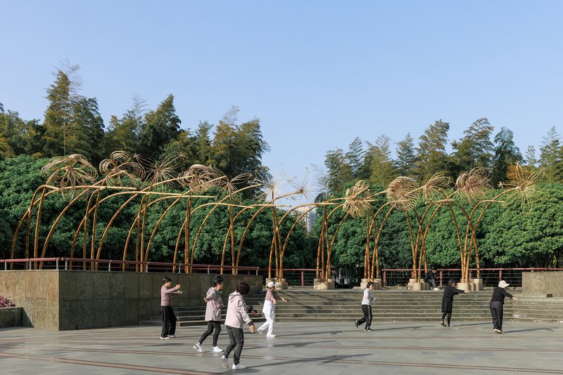 Bamboo canopy installation on a terraced plaza with visitors exercising beneath the curved ribs in daylight