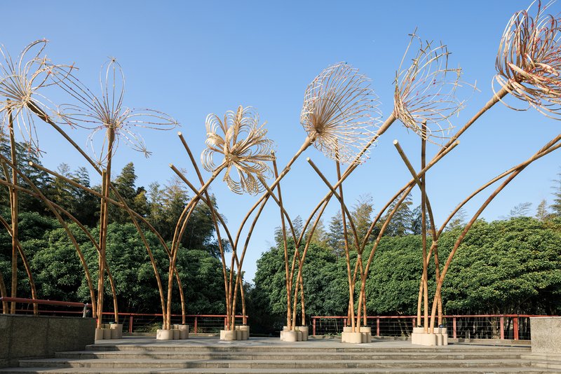 Sculptural bamboo installation with woven wire flower forms rising from concrete bases on stepped plaza