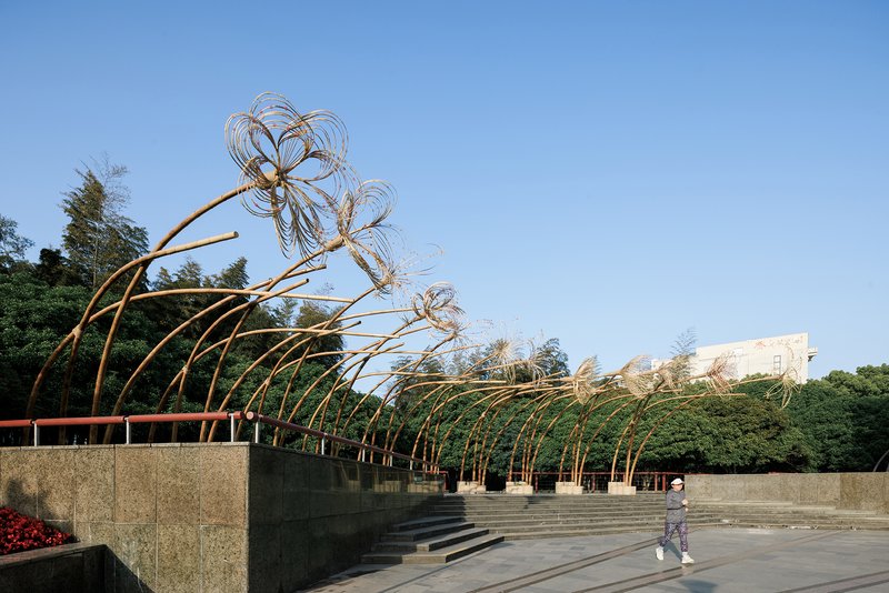 Arching bamboo structures with wirework canopies along terraced plaza as visitor crosses the space