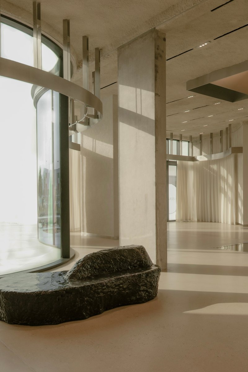 Interior with raw volcanic stone basin beneath tall windows and vertical concrete fins in soft daylight