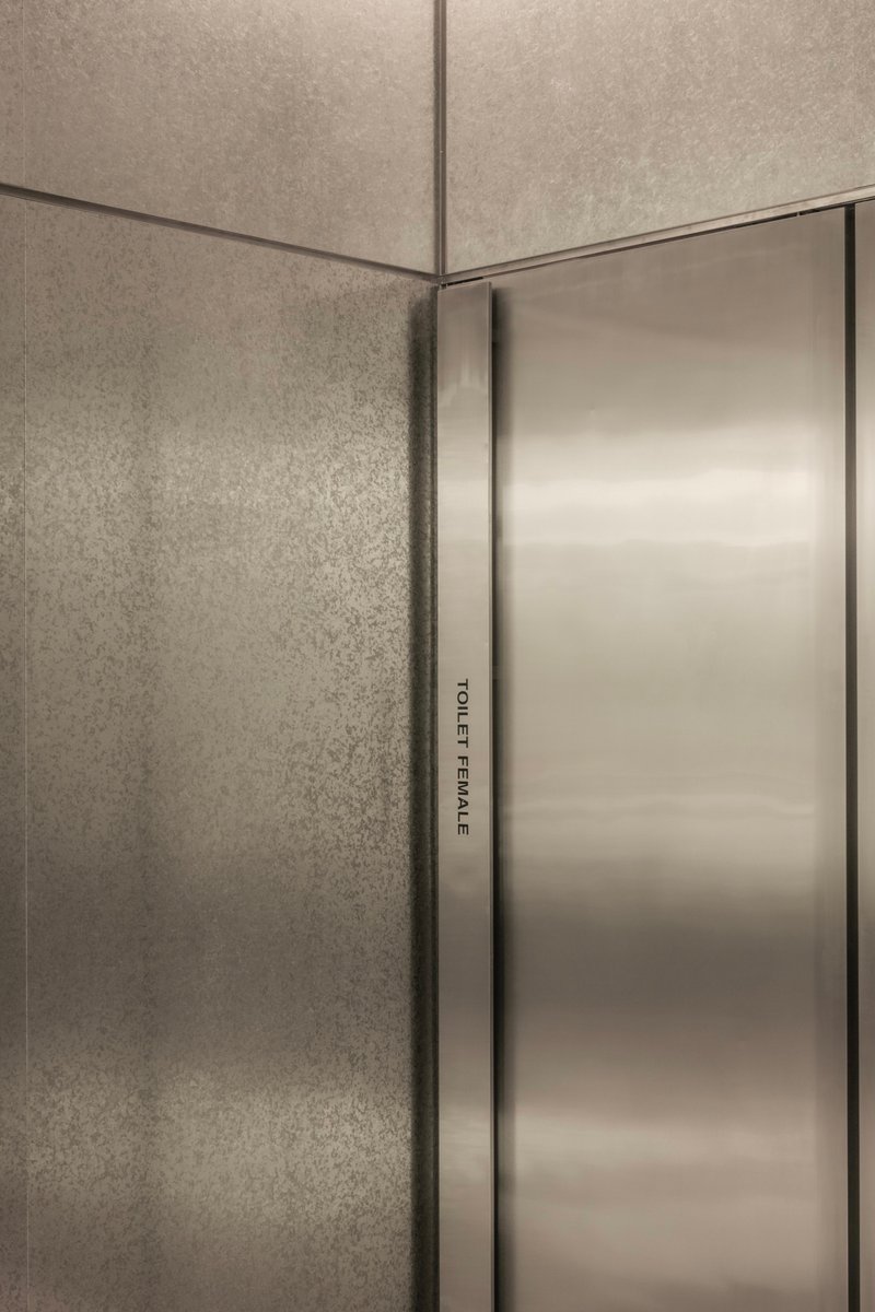 Close-up of brushed stainless steel door edge against textured concrete wall corner