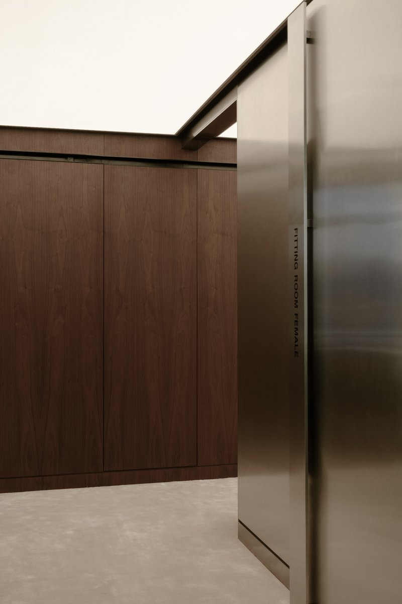Detail of walnut-paneled wall meeting brushed metal door frame under a concrete soffit