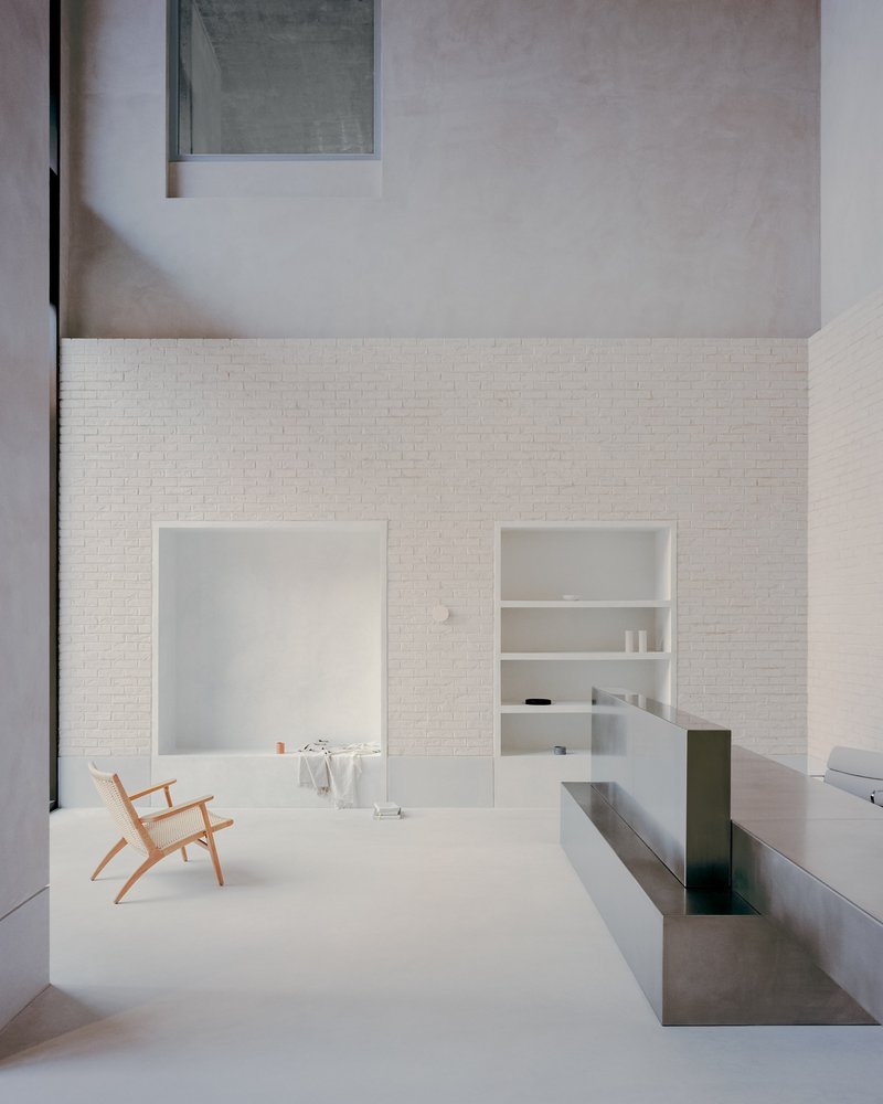 Double-height courtyard with white brick walls and a timber chair on pale flooring
