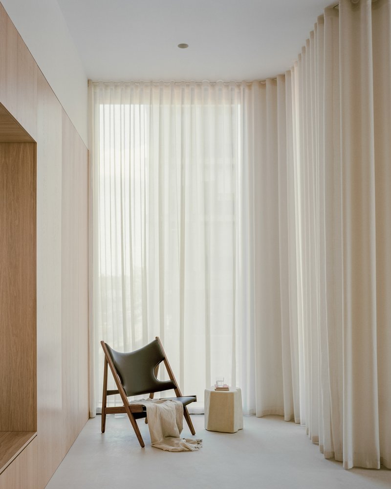 Curved alcove with floor-to-ceiling sheer curtains filtering daylight beside a walnut lounge chair