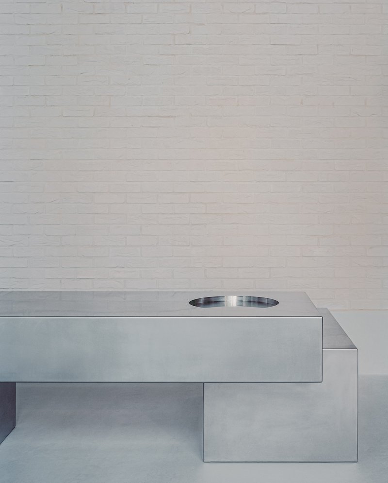 Cantilevered stainless steel countertop with circular basin against white painted brick wall