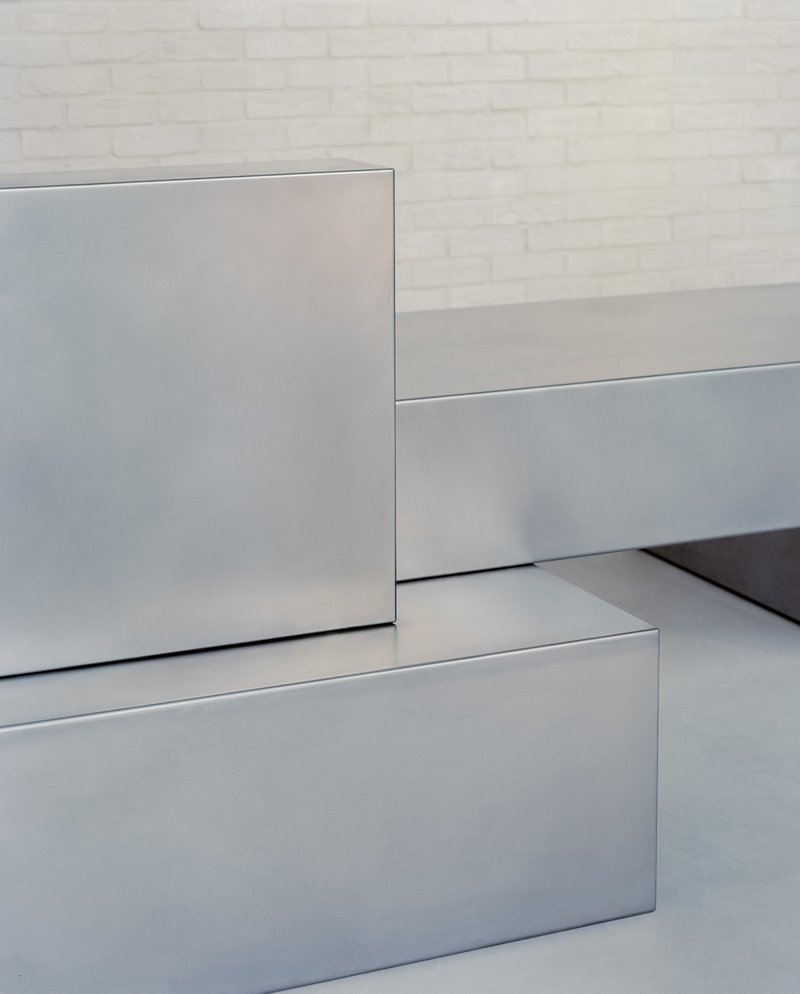 Detail of stainless steel counter edges and joints meeting white brick wall and grey flooring