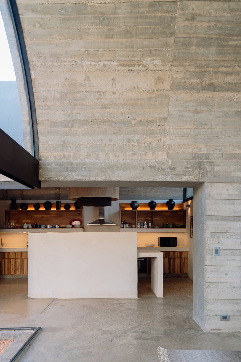 Board-formed concrete wall rising above a white plaster kitchen island with timber cabinets