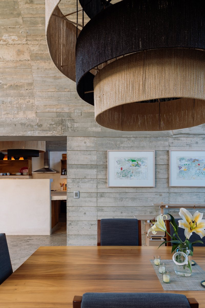 Layered timber pendant lights suspended from a board-formed concrete ceiling above the dining table