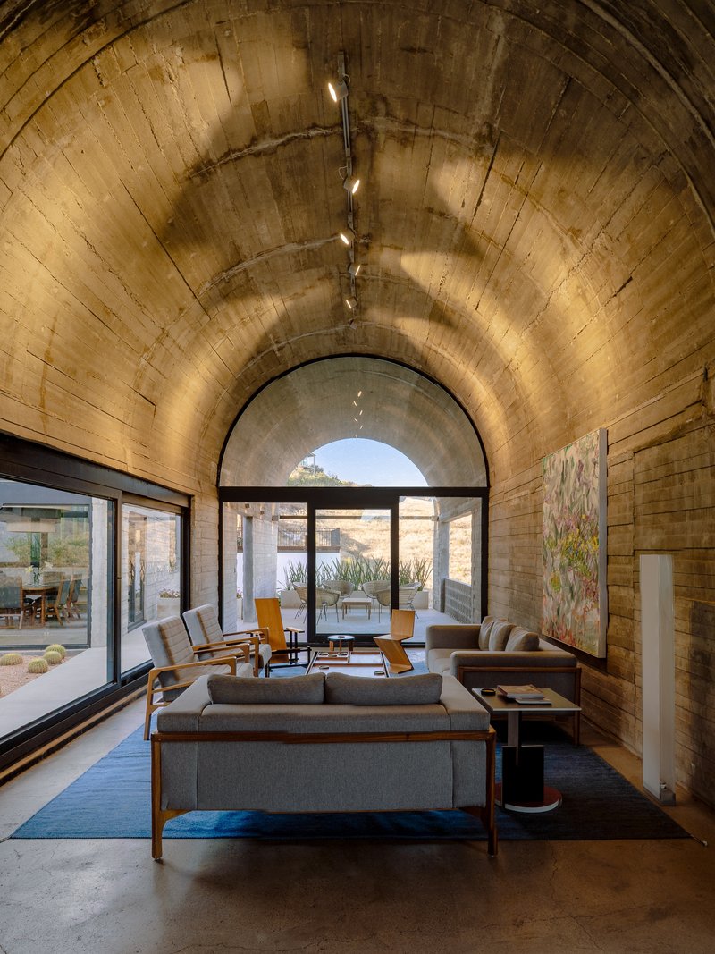Living room under a board-formed concrete barrel vault with arched glazing to the courtyard