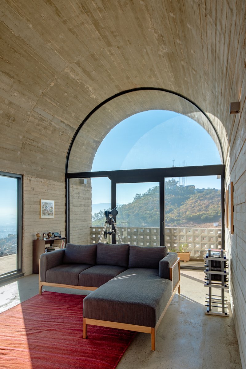 Seating area beneath a board-formed concrete arch with hillside views through the black-framed glazing