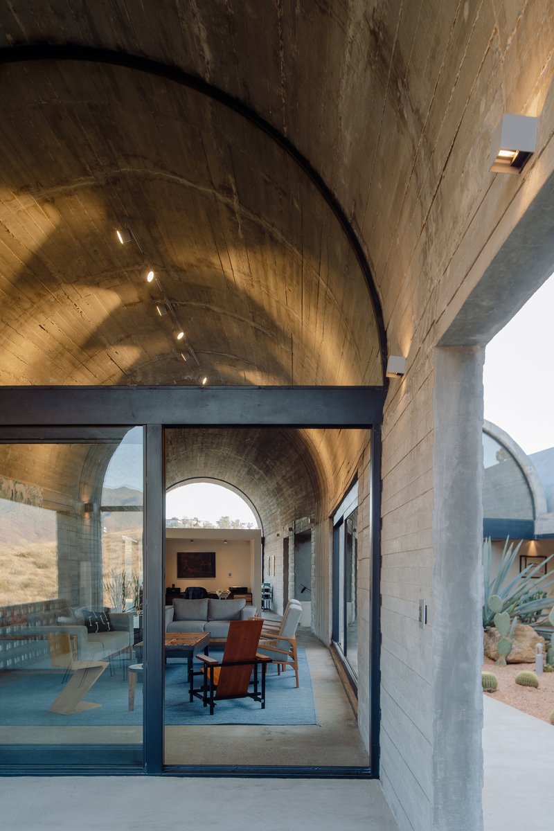 Barrel-vaulted board-formed concrete ceiling over an open living space with full-height glass walls and desert landscape beyond