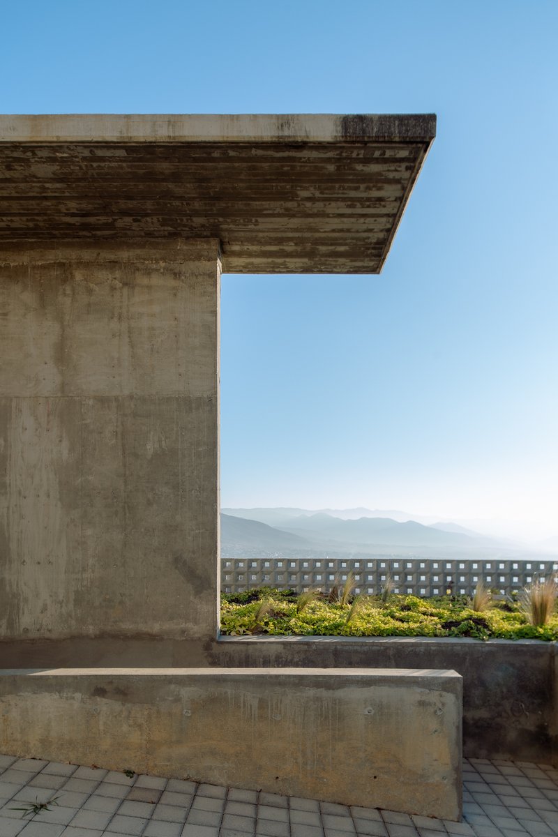 Rooftop terrace with board-formed concrete canopy and planted bed framed by perforated screen wall and distant hills