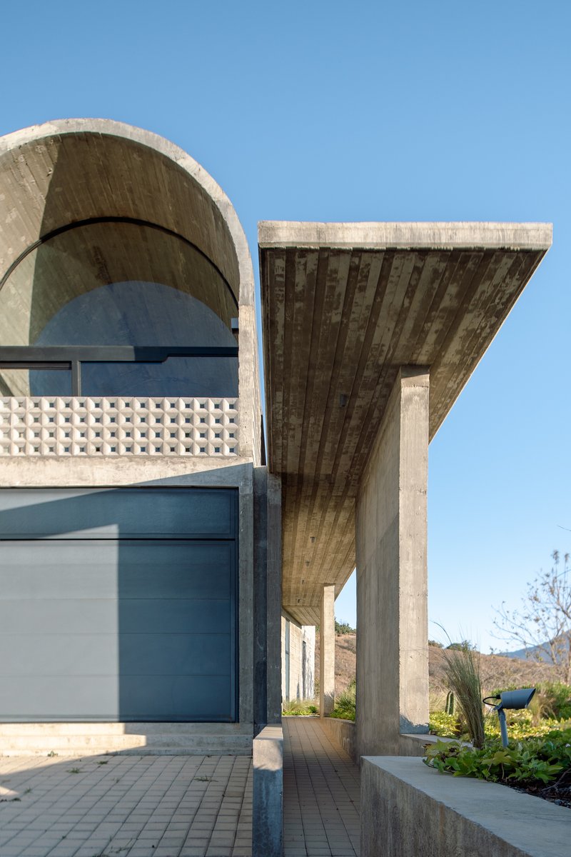 Close-up of arched vault edge meeting cantilevered concrete canopy with board-formed soffit under clear sky