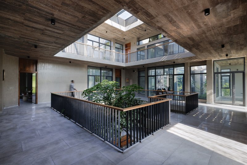 Central courtyard with planted bed surrounded by vertical slat railings beneath an exposed concrete ceiling and skylight