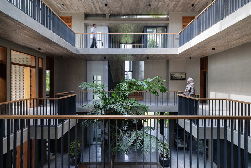 Three-story atrium with vertical slat balustrades and central tree planters with figure standing on upper gallery