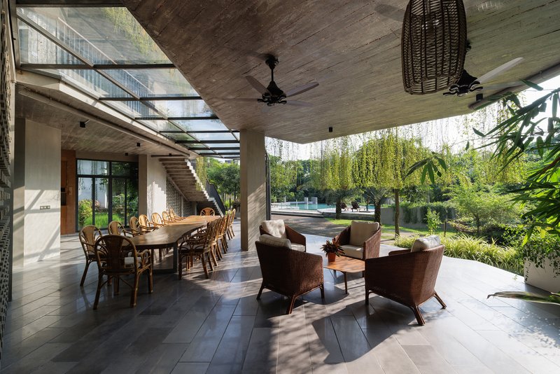 Covered terrace with dining table and lounge seating beneath board-formed concrete soffit and steel skylight