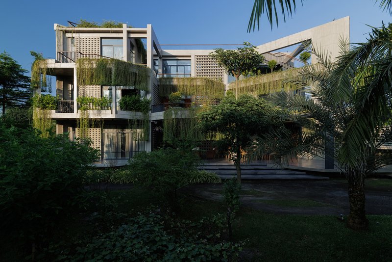 Garden facade showing stacked balconies with perforated concrete screens and hanging greenery among palm trees at dusk