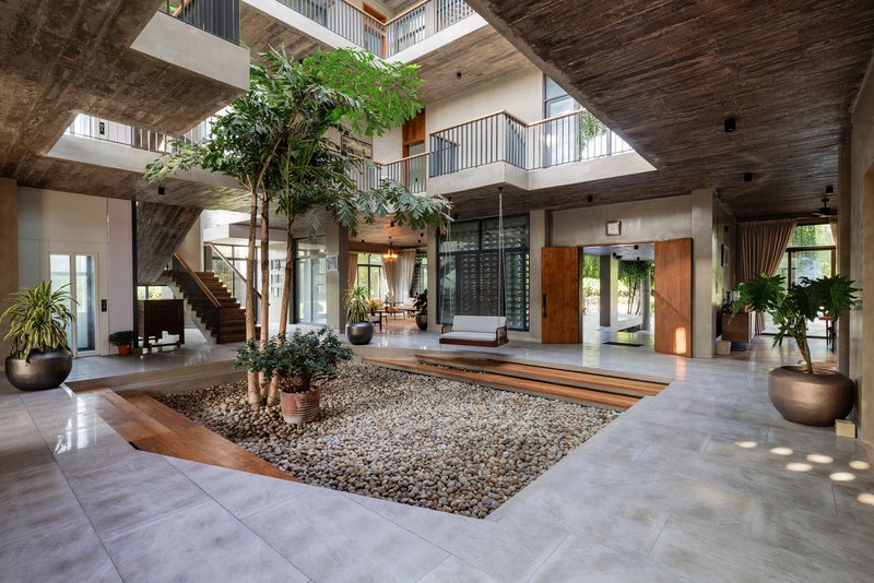 Double-height interior courtyard with sunken gravel garden, potted trees, and timber-clad ceiling with skylight above