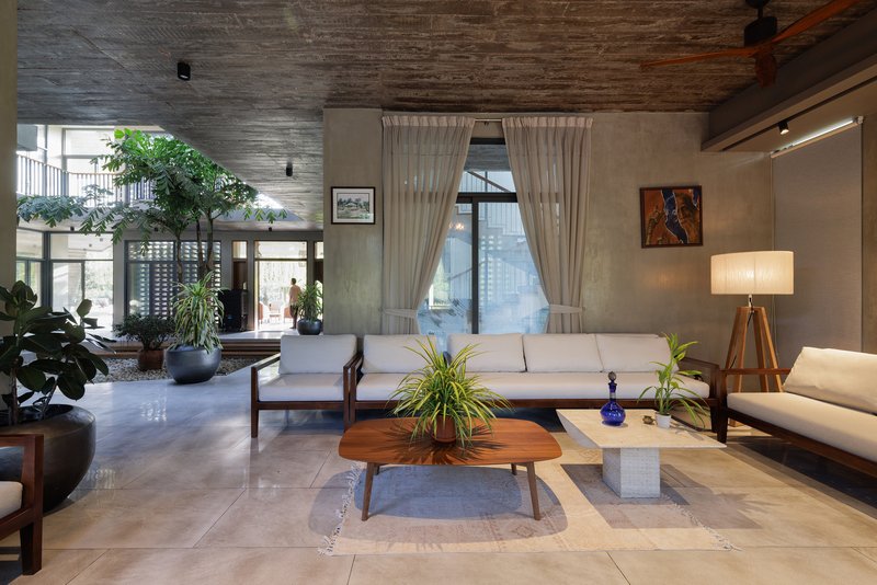 Living room with timber ceiling, potted plants by glazed walls and low sofas on stone flooring
