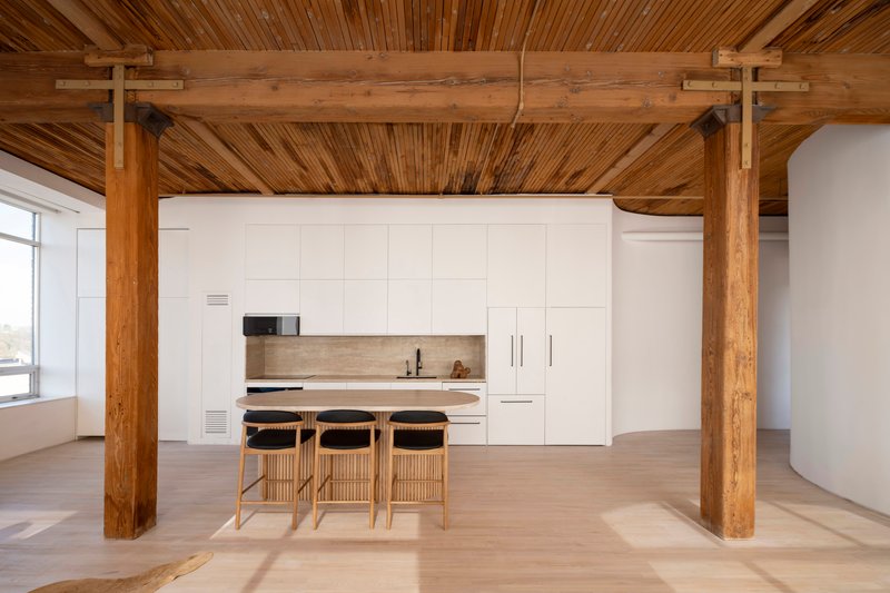 Kitchen area framed by exposed timber beams and columns with slatted wood ceiling in afternoon light