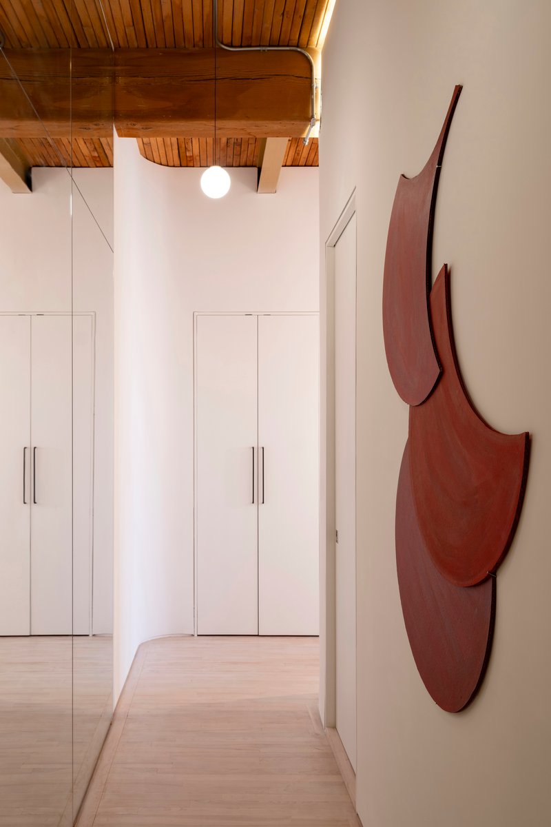 Corridor with tall white storage cabinets and curved red wall sculpture under coved ceiling