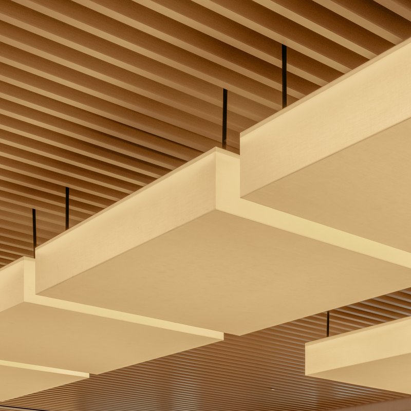 Detail view of layered pale panels suspended by black rods below the ribbed timber ceiling