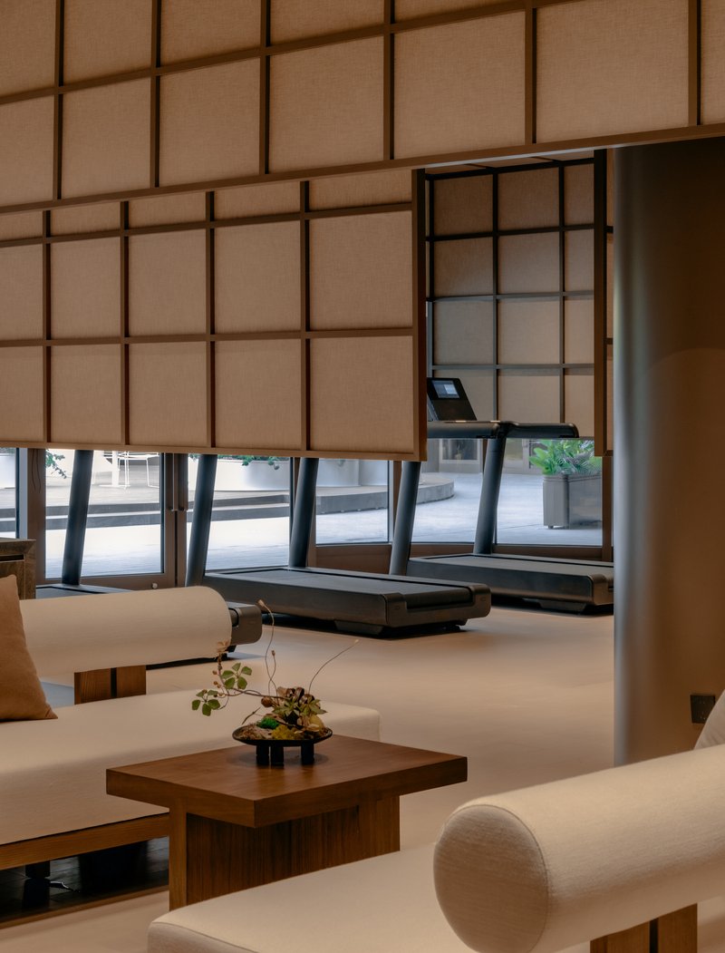 Corner seating area with low timber table and bonsai plant beneath gridded translucent wall panels