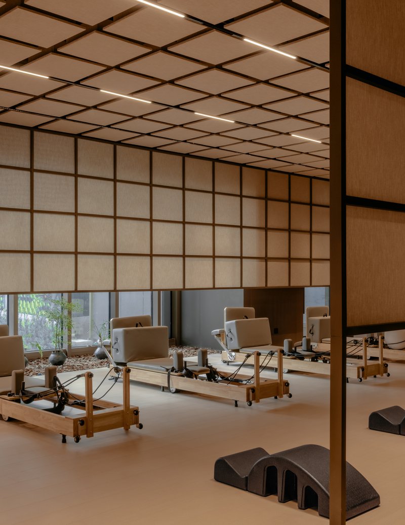 Pilates studio with wooden Reformer machines on pale floor beneath gridded translucent ceiling panels