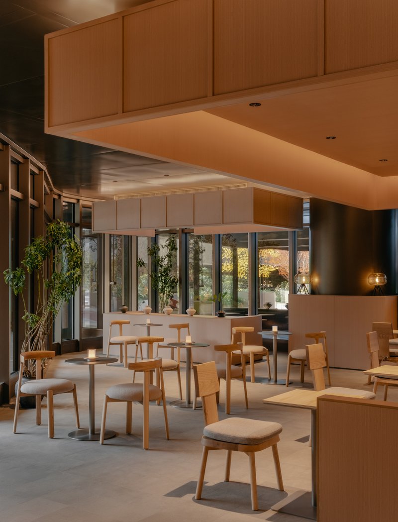 Dining zone under floating timber ceiling plane with glass wall revealing courtyard vegetation at twilight
