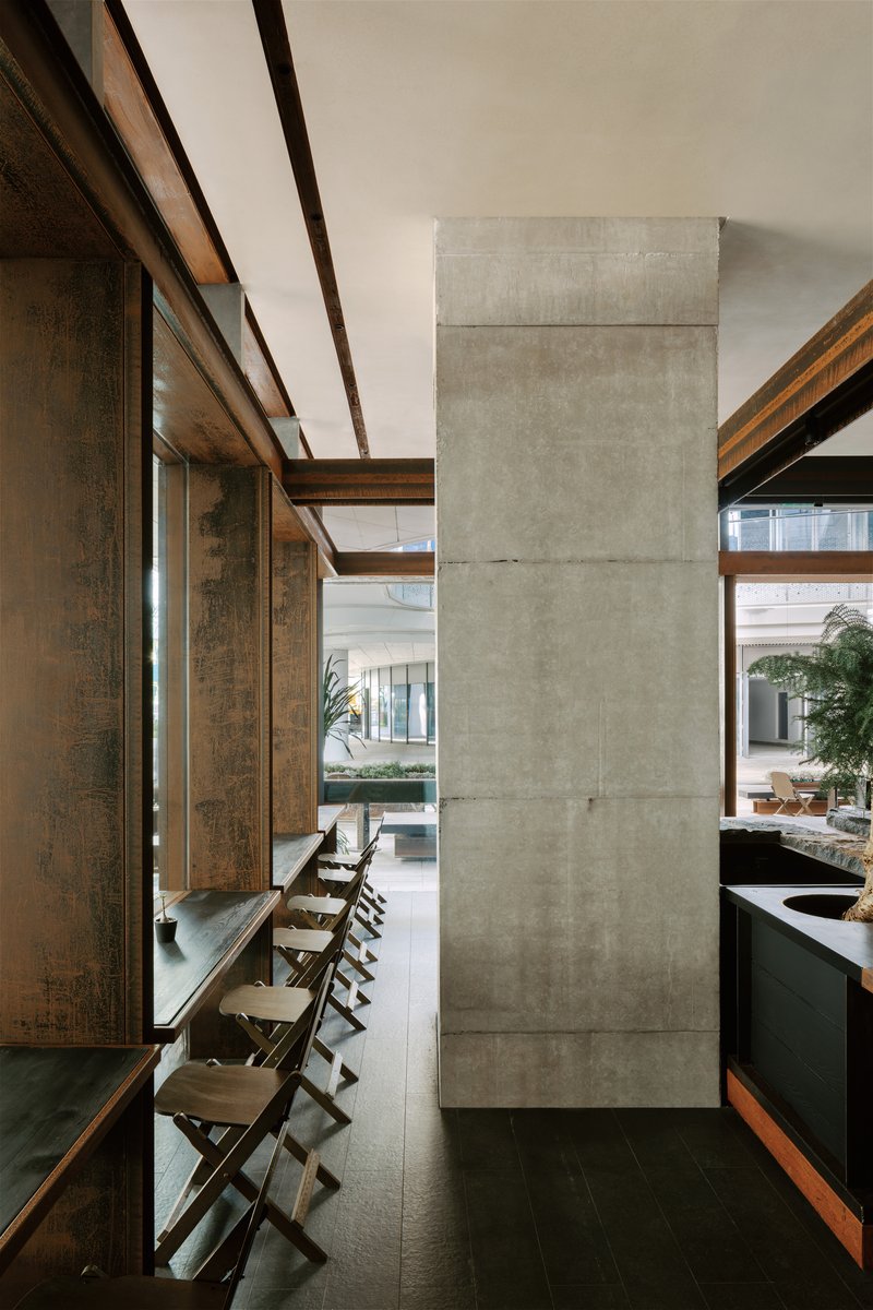 Poured concrete column beside a timber-framed wall with folding chairs along a narrow ledge