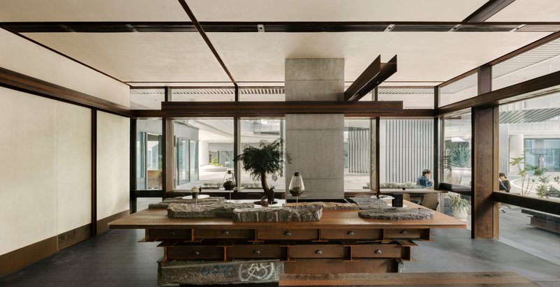 Wide view of the communal table with stone surfaces surrounded by glazed walls opening to courtyard