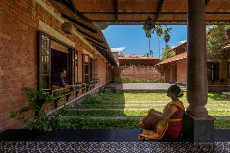 Covered veranda with exposed timber beams where two people sit facing the grass courtyard