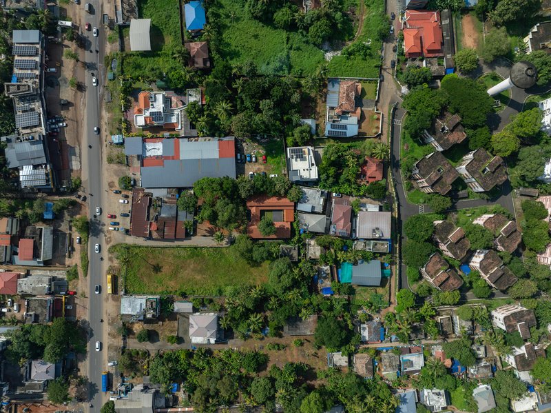Drone view of dense residential neighborhood showing varied roof colors and tree canopy between houses and streets