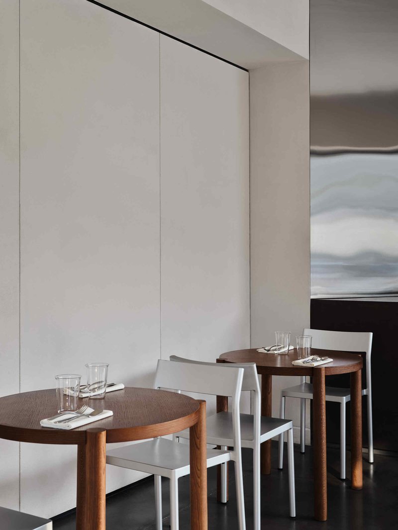 Dining area detail with round timber tables, pale metal chairs, and soft daylight through translucent panels