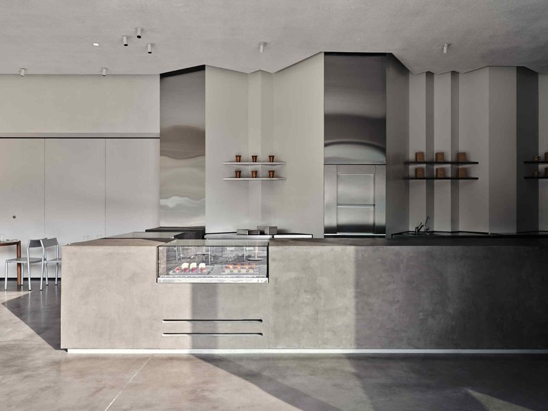 Concrete service counter with integrated display case and stainless steel exhaust hood in a cafe interior