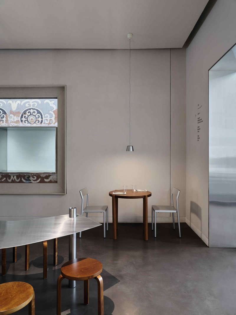 Seating alcove with pendant light illuminating a wooden table and aluminum chairs beside a framed window opening
