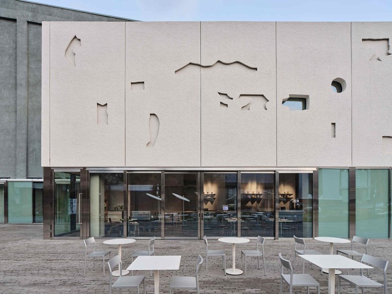 Close-up of the paneled facade with abstract cutouts revealing glimpses of the interior through glazing below