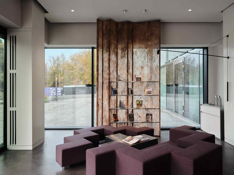 Interior lounge with purple modular seating facing a central wood-clad shelving wall flanked by full-height glazing