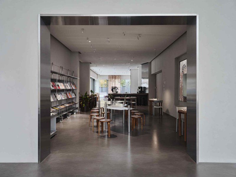 View through a wide doorway into a gallery space with metal bookshelves and wooden seating under track lighting