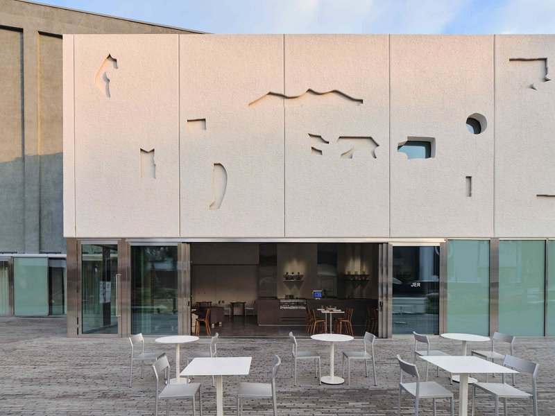 Evening view of the textured facade panels with cutout silhouettes illuminated from within above the glazed entrance