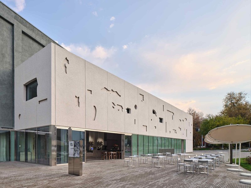 Exterior view of the white panel facade with irregular cutout windows above a continuous glazed ground floor terrace